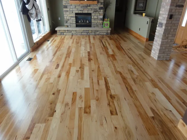 Light oak floor in a living room with a stone fireplace and large windows